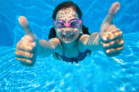 Young girl under water with thumbs up towards the camera.