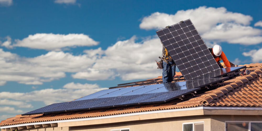 Two men on a roof of a house installing solar panels.