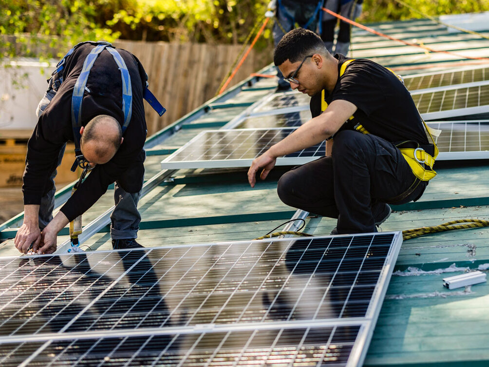 Two men on a roof installing solar panels.